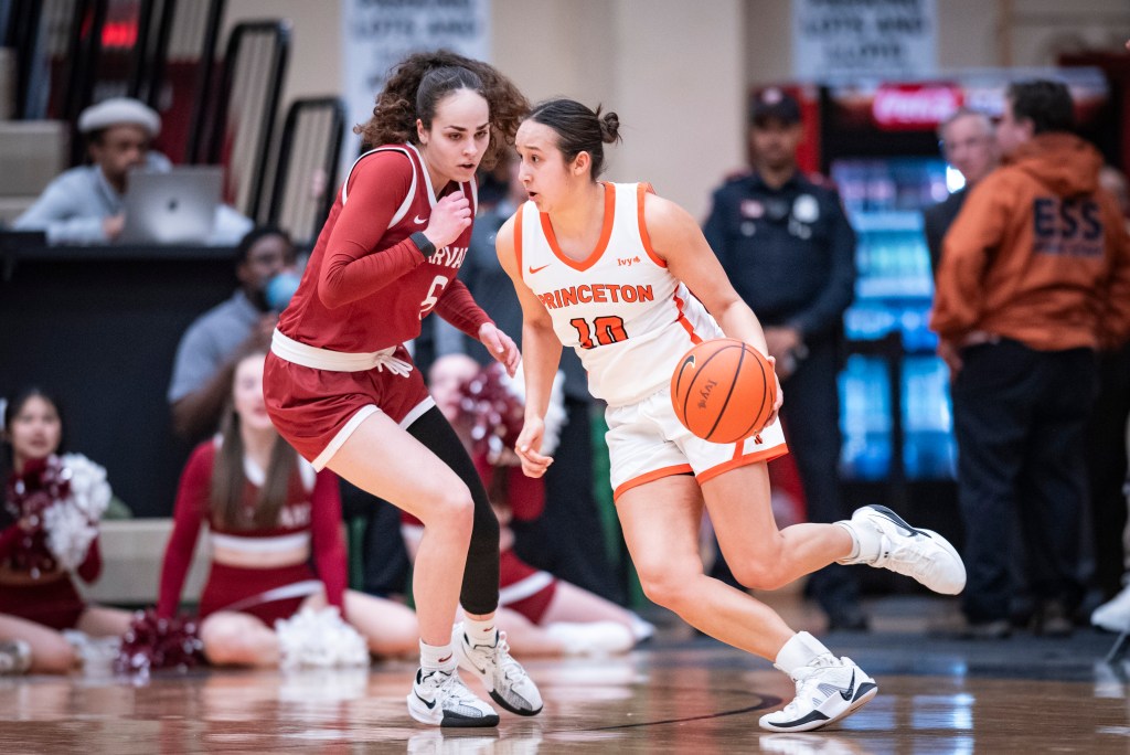 Princeton guard Skye Belker dribbles the ball with her left hand on the perimeter. Harvard guard Lydia Chatira slides her feet to try to stay with Belker.