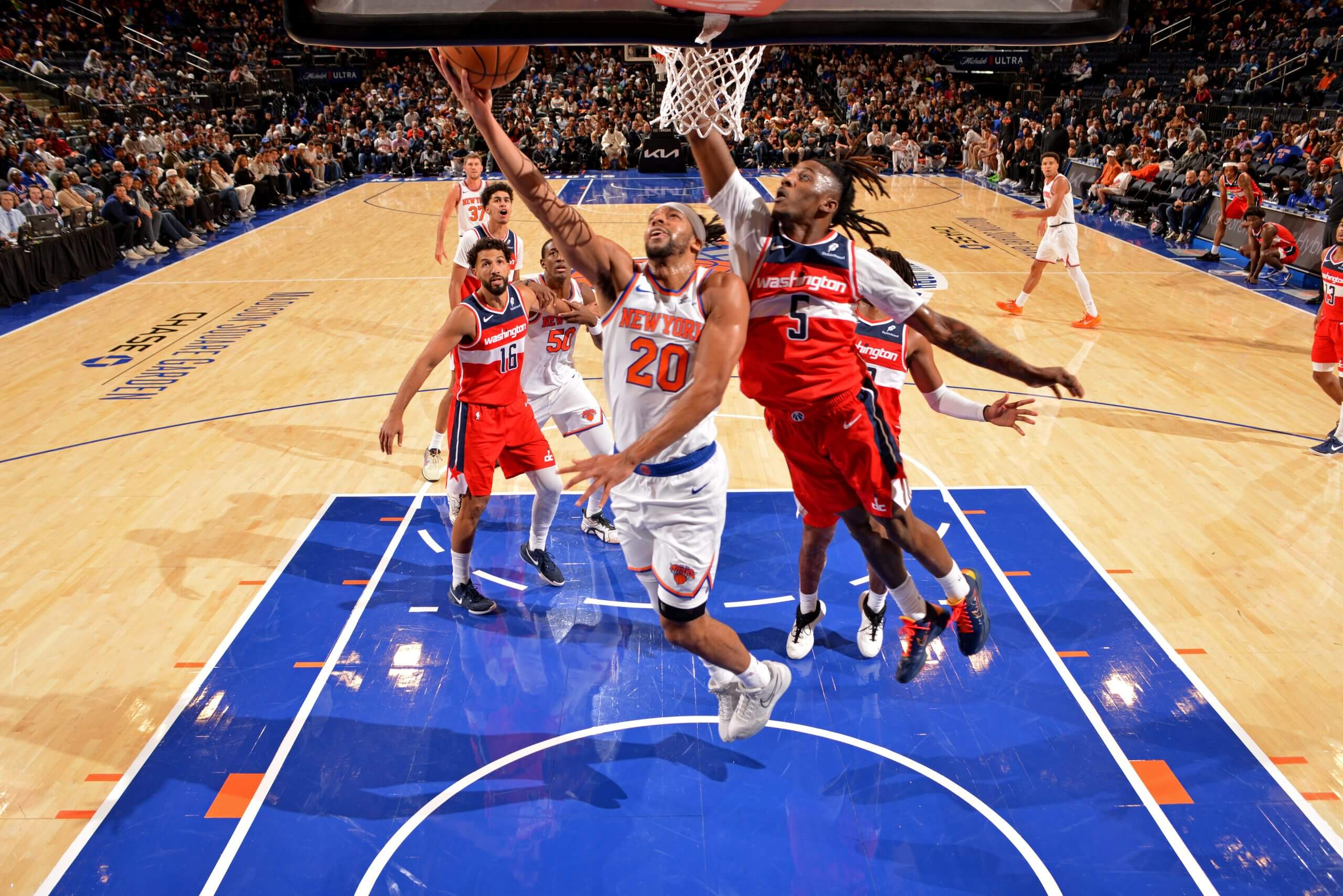 The New York Knicks' Tosan Evbuomwan, wearing No 20, jumps into the air as he drives to the basket under pressure from a Washington Wizards opponent