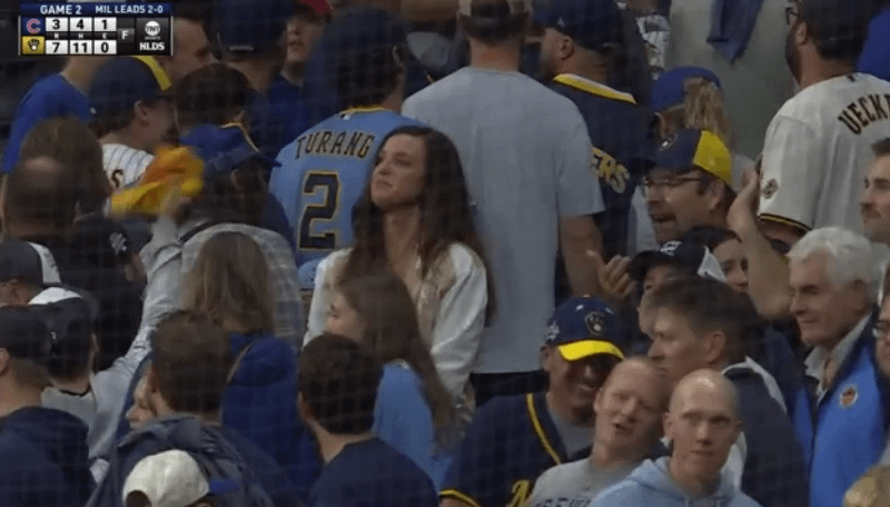 A lady standing still among the moving crowd looking incredibly proud as the Brewers take game 2 against the Cubs