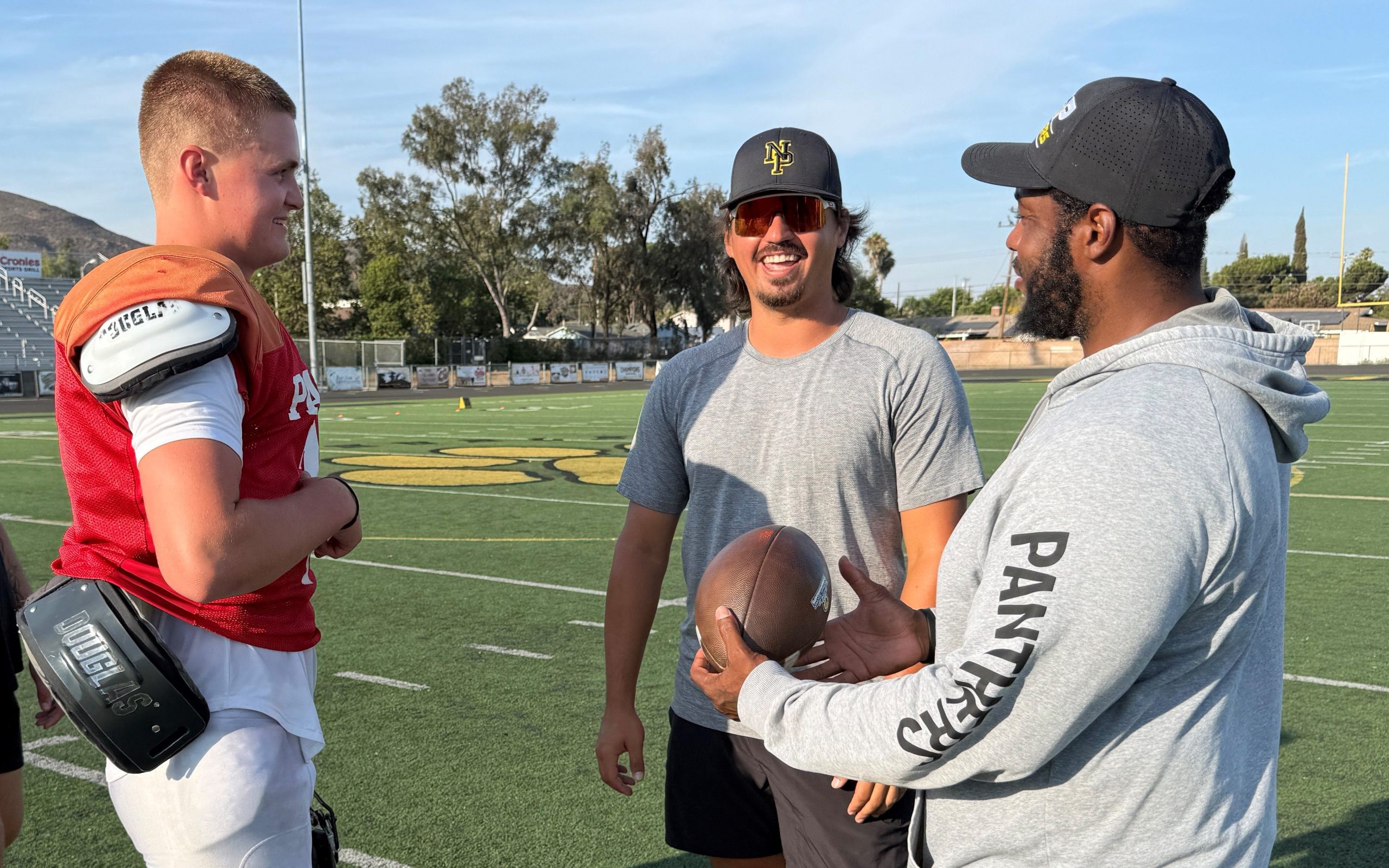 Brady Smigiel, in an orange-reddish practice jersey, chats with a smiling Cam Rising and Whitney Lewis during an August practice.