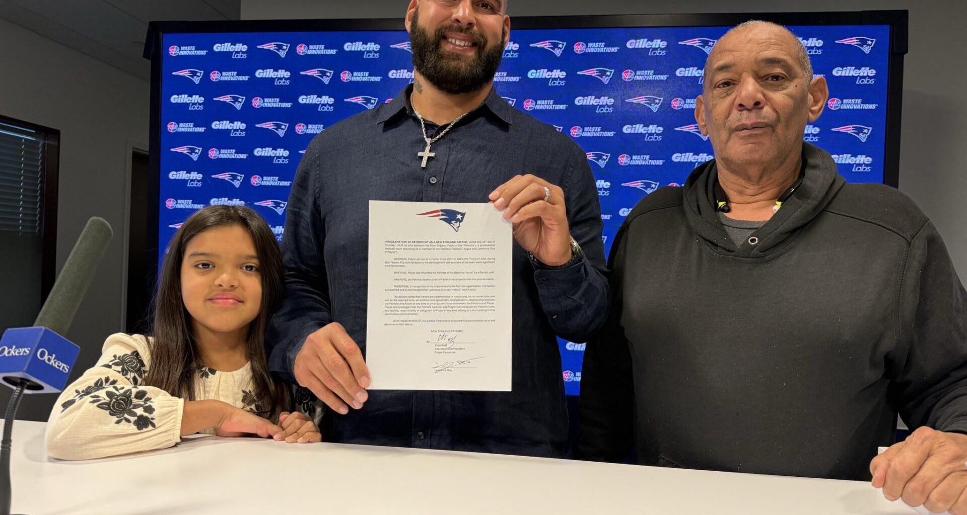 [Mike Reiss] Lawrence Guy holds up his ceremonial one-day contract, standing alongside his daughter Adriana and his father Michael.