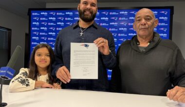[Mike Reiss] Lawrence Guy holds up his ceremonial one-day contract, standing alongside his daughter Adriana and his father Michael.