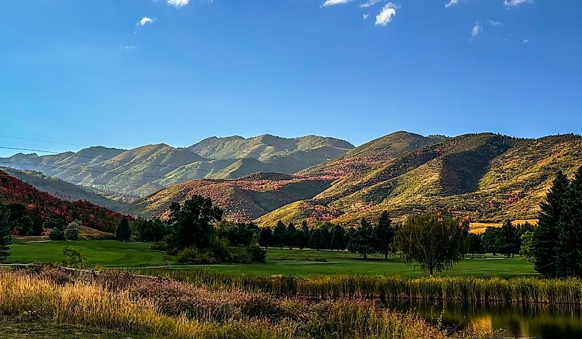 View of mountains spotted with leaves of fall colors; pond and golf course in the foreground; autumn in Wasatch Mountain State Park
