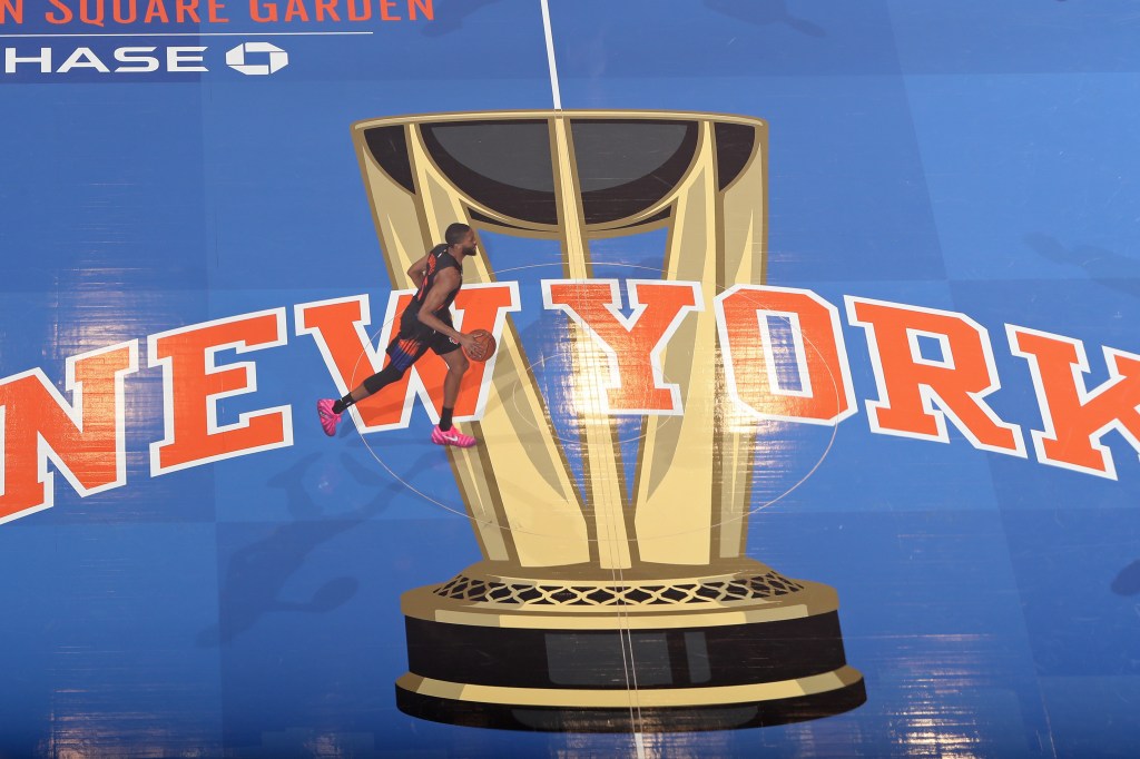 Mikal Bridges of the New York Knicks handles the ball on a blue court with a large golden cup and "NEW YORK" in orange letters.