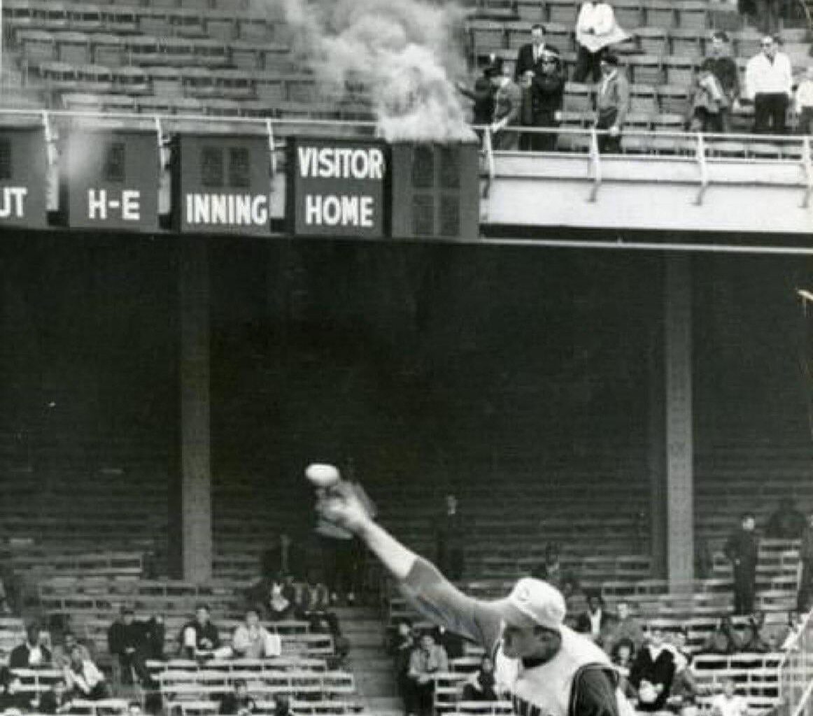 The scoreboard at Connie Mack Stadium burns as Jim Maloney pitches with Pete Rose in the background, April 16, 1966.