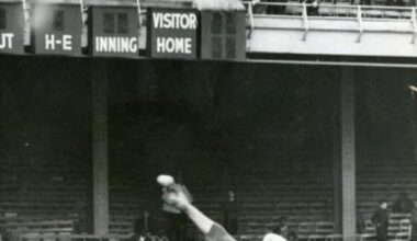 The scoreboard at Connie Mack Stadium burns as Jim Maloney pitches with Pete Rose in the background, April 16, 1966.