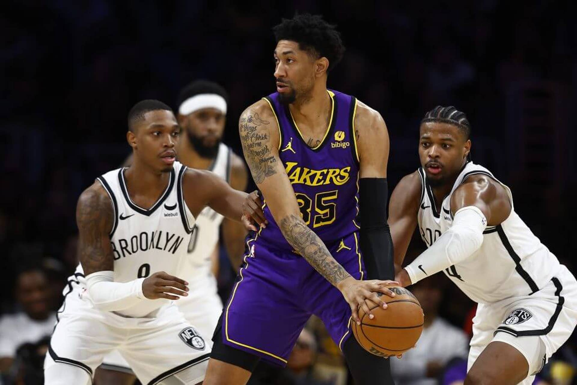 Lakers' Christian Wood holds the ball while two Nets players defend him during an NBA game.