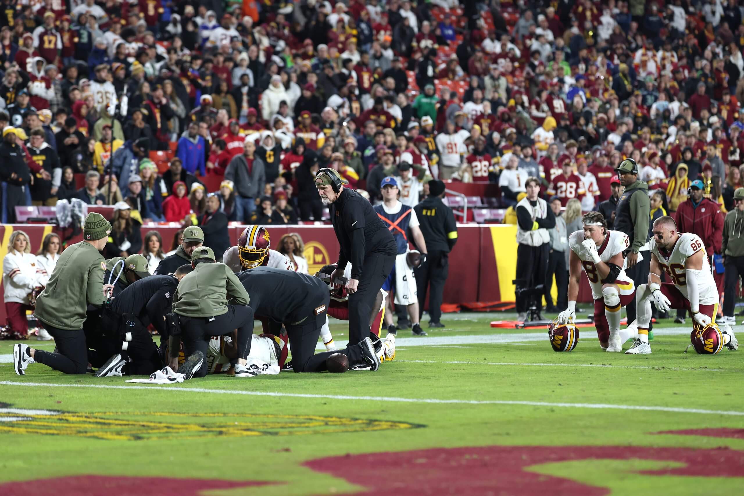 The Commanders kneel as medical staffers tend to injured quarterback Jayden Daniels. 