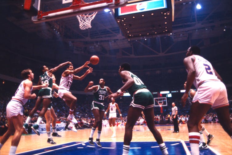 A player holding basketball jumps in air as opposing team tries to block a pass.