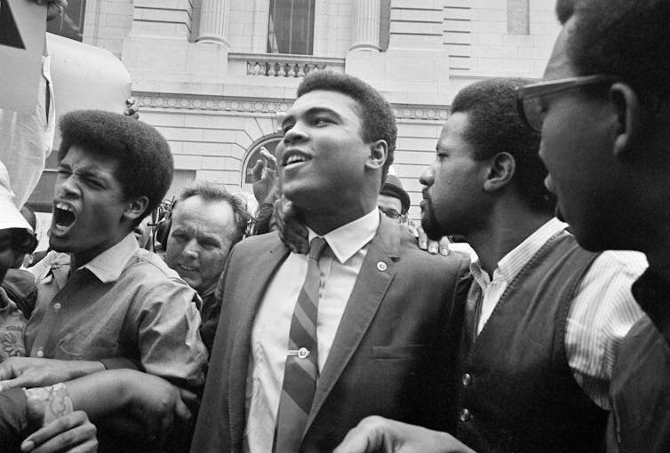 Black and white photo of man in suit and tie surrounded by crowd