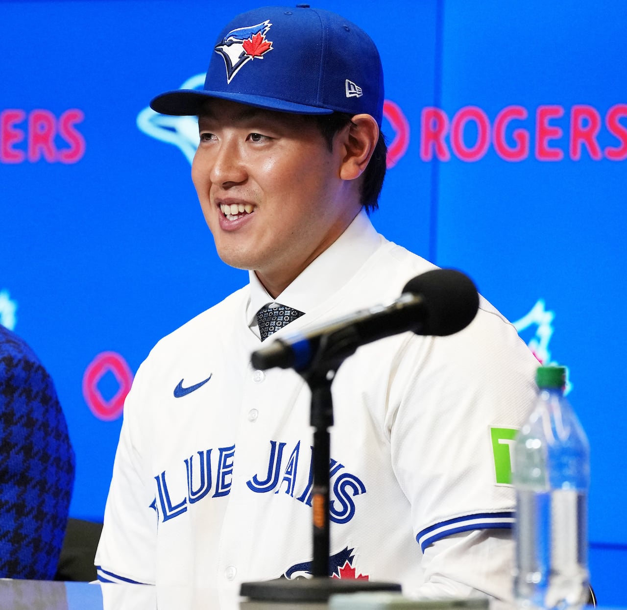 A man smiling, while wearing a Blue Jays jersey and baseball cap