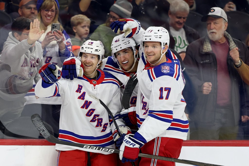 Three New York Rangers players smiling on the ice during a game.