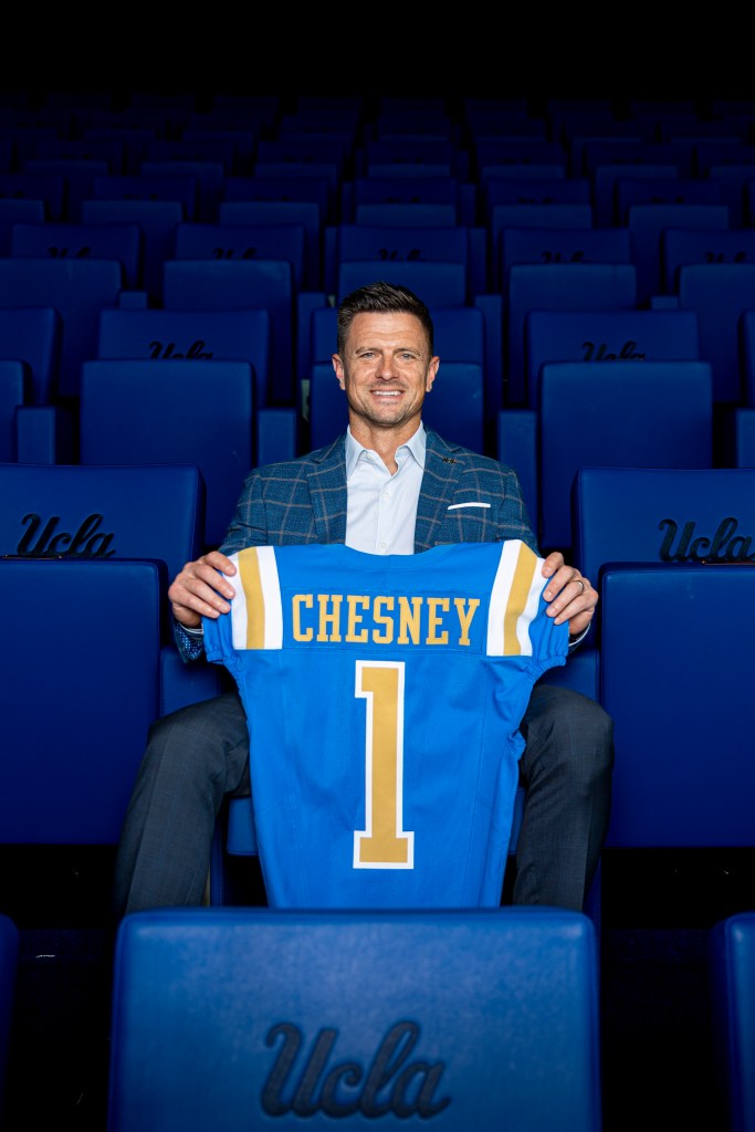 UCLA FB head coach Bob Chesney holding a blue jersey with "CHESNEY" and the number "1" on the back.