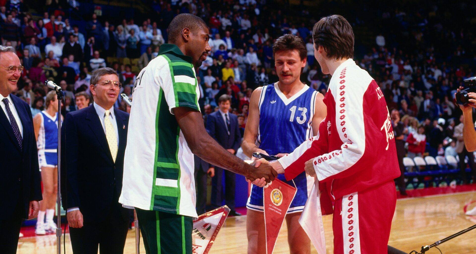 Basketball players from different teams shake hands at center court while officials and other players observe during a pre-game ceremony.