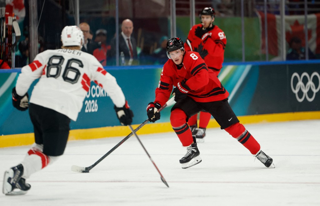 Cale Makar of Canada in red and Janis Moser of Switzerland in white during an ice hockey game.