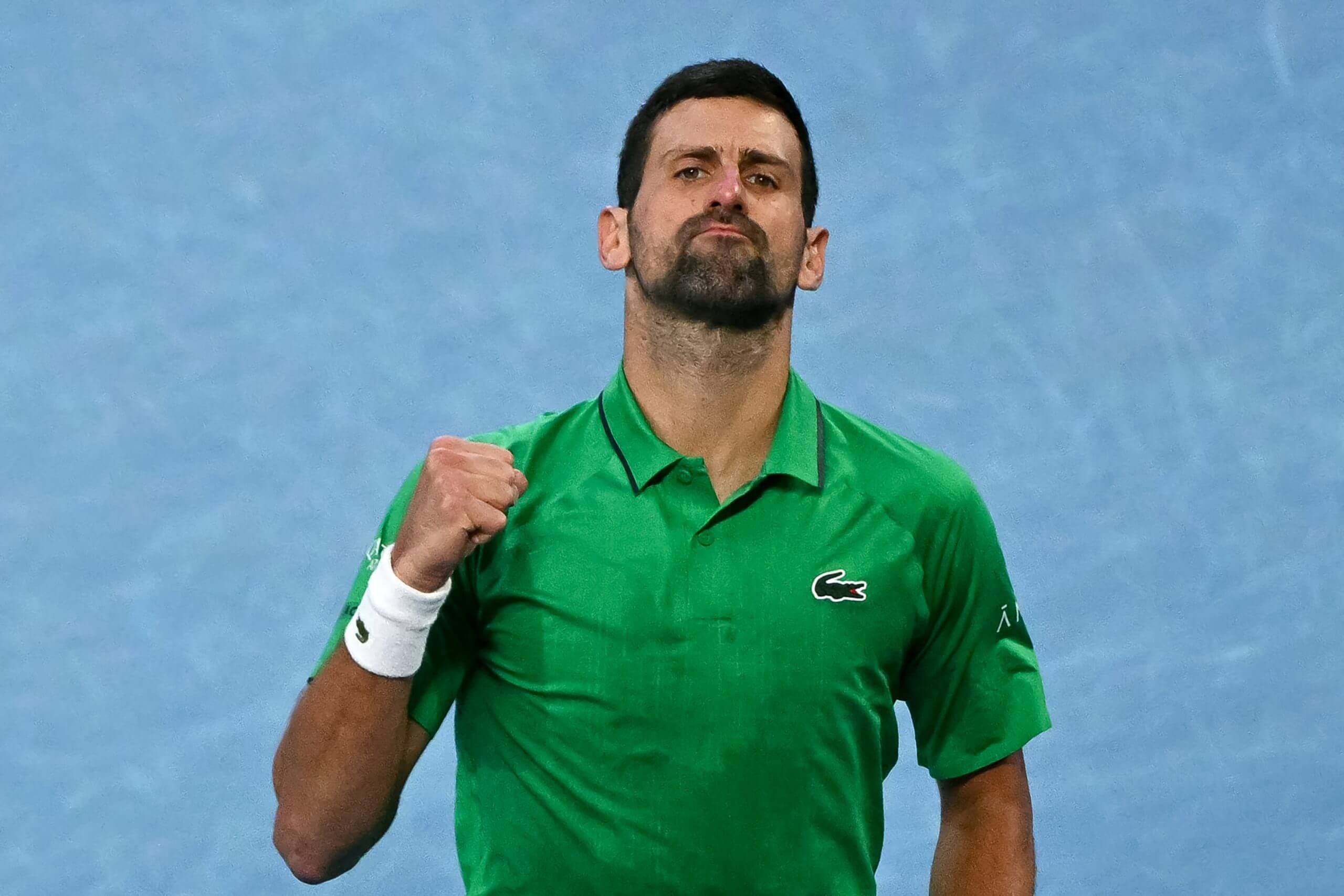 Novak Djokovic pumps his fist and wears an expression of defiance on a blue tennis court.
