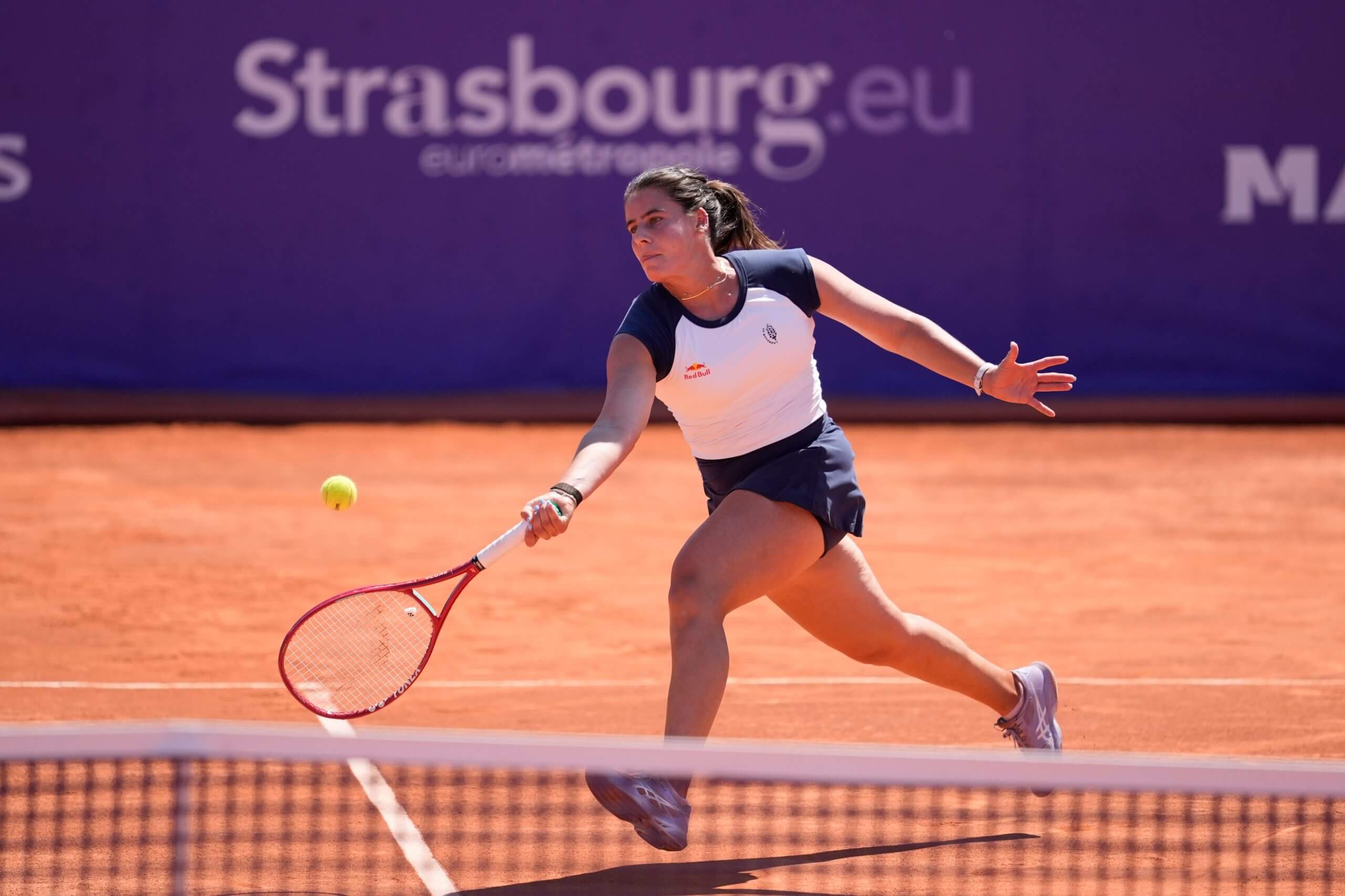 Emma Navarro moves forward to hit a forehand on a clay tennis court.
