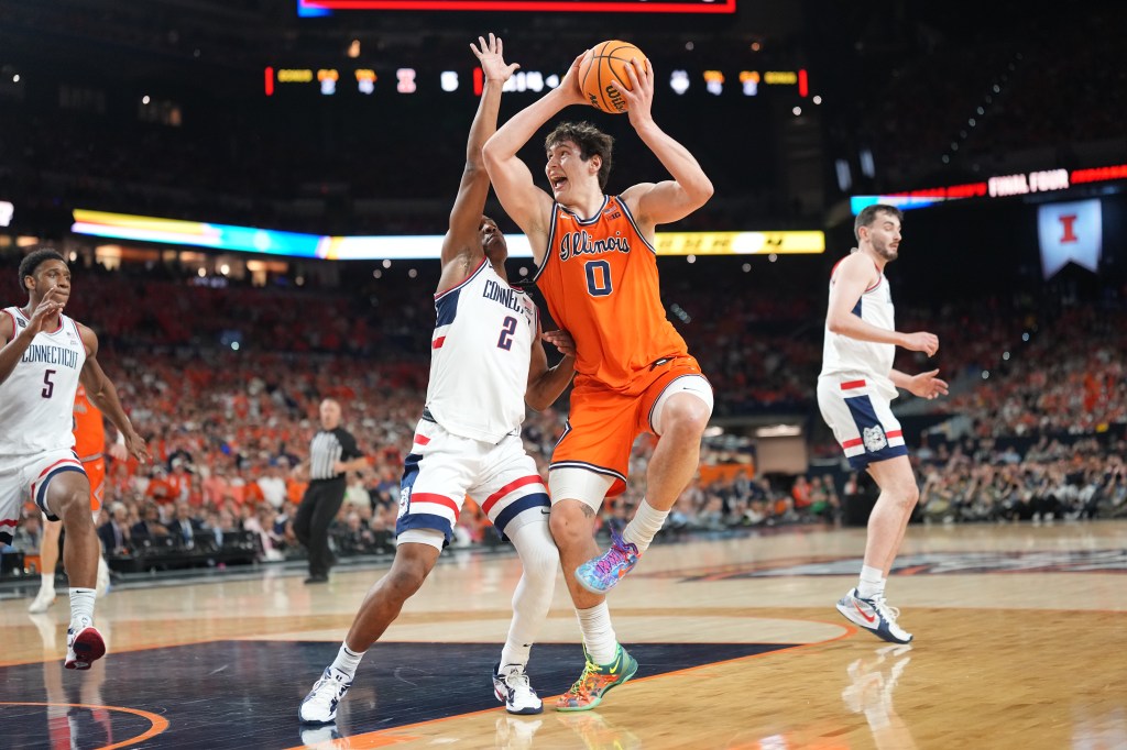 A University of Illinois player in orange (jersey #0) attempts a shot against a University of Connecticut player in white (jersey #2) during the 2026 NCAA National Semifinals.