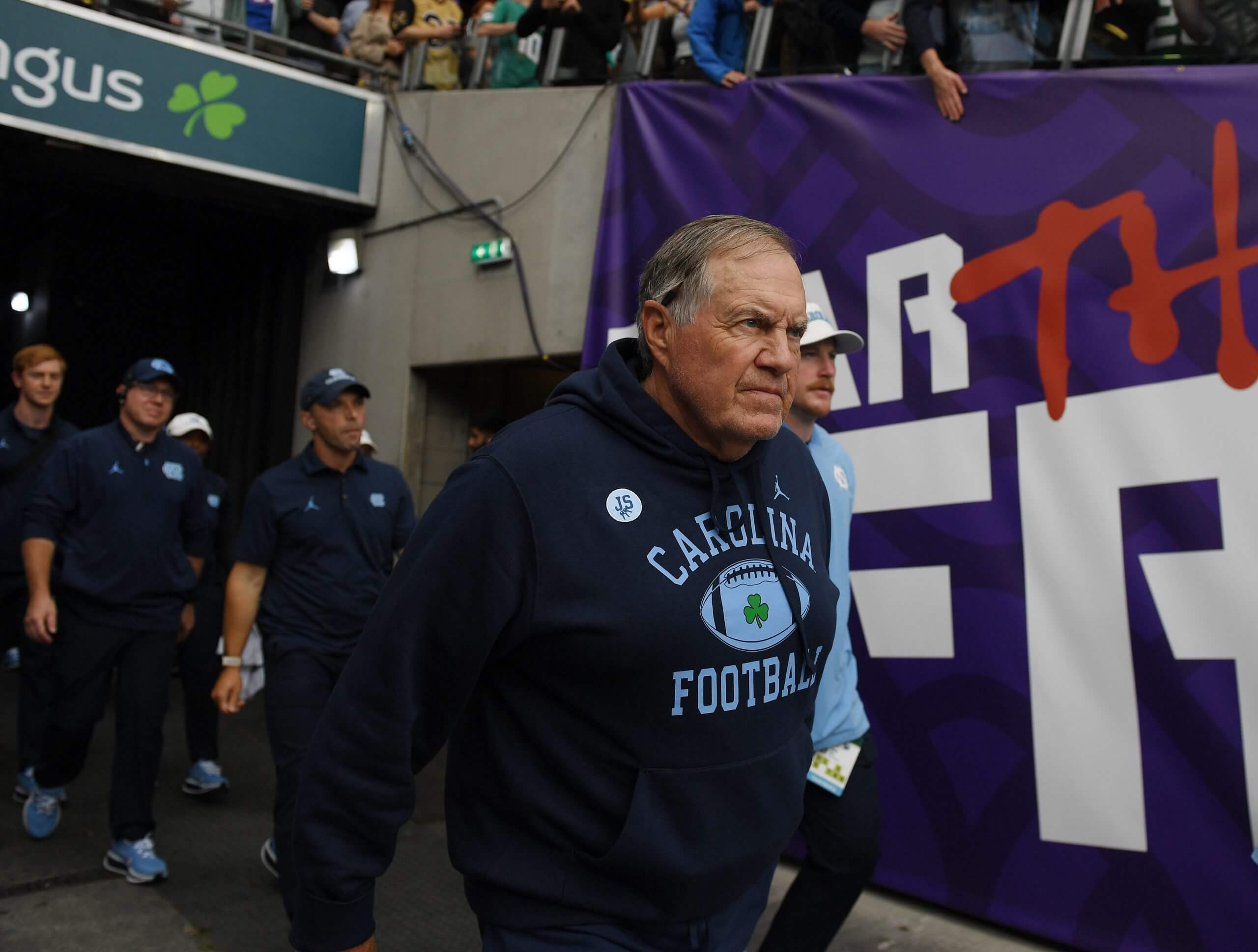 Bill Belichick, wearing a Carolina Football sweatshirt, walks through the tunnel onto the field