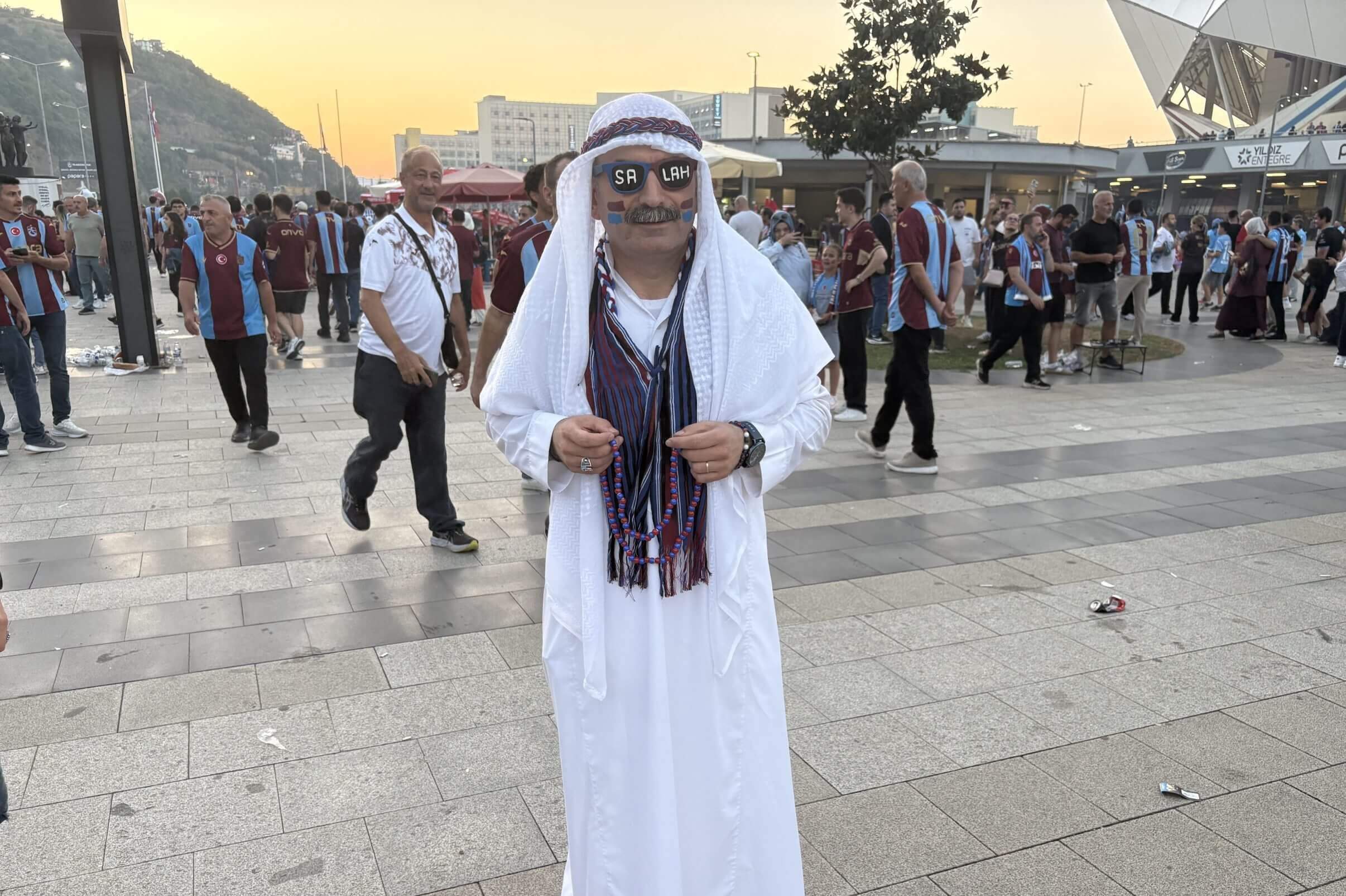 A Trabzonspor supporter wears a white robe and sunglasses adorned with "Salah" ahead of Trabzonspor's game against Ferencvaros