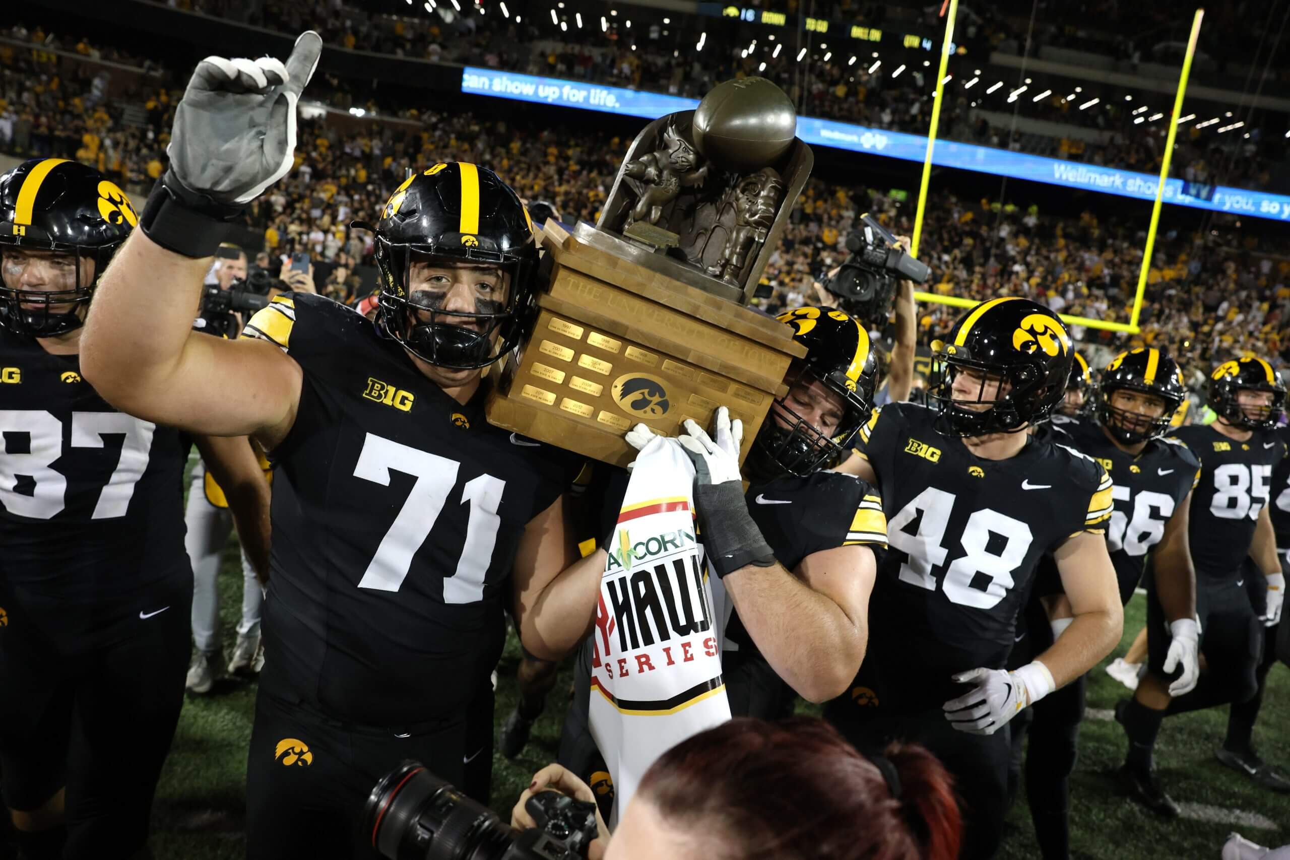 Iowa offensive linemen Jack Dotzler and Trevor Lauck (59) carry the Cy-Hawk Trophy off the field with teammates behind them