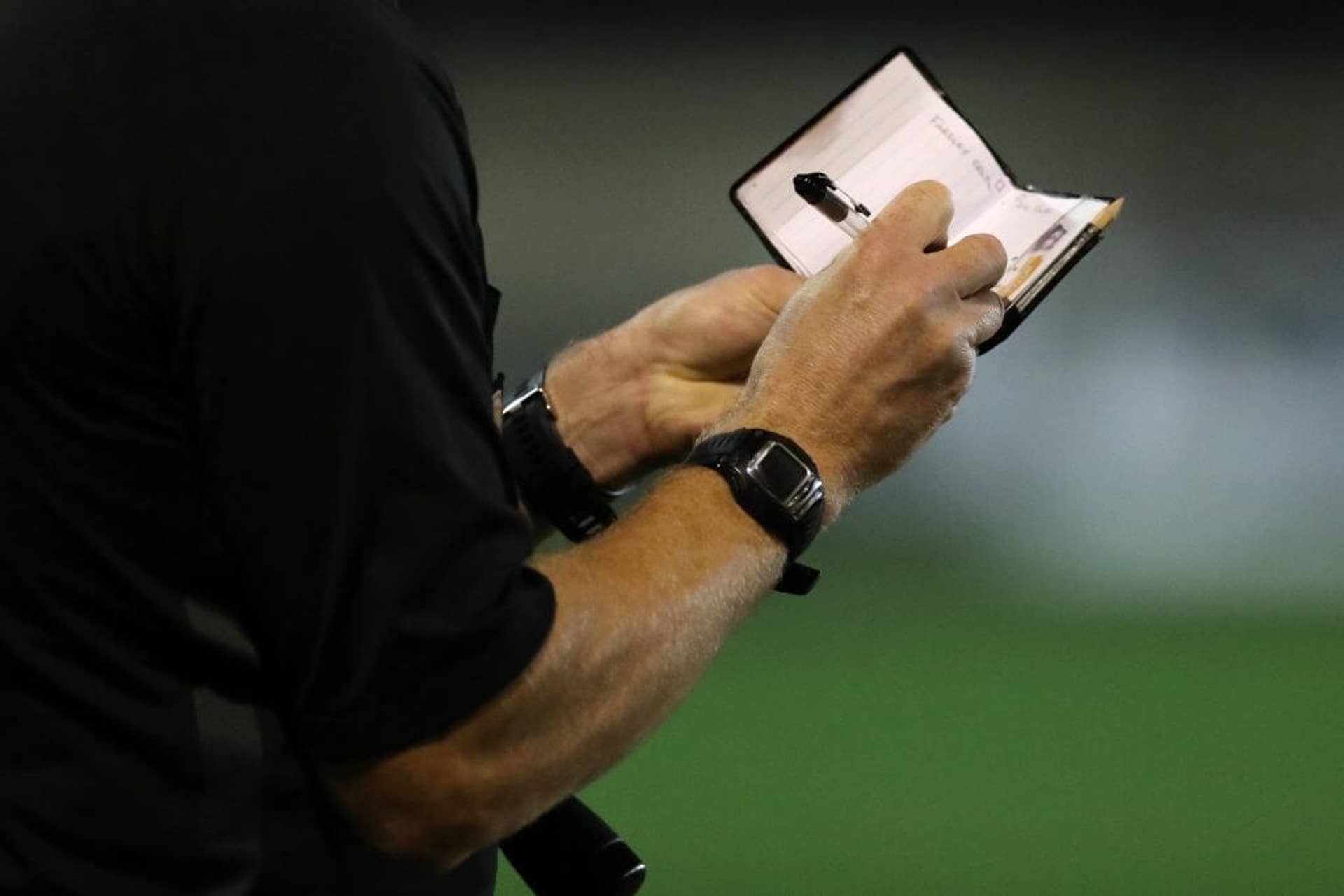Side image of a football referee writing notes in a book
