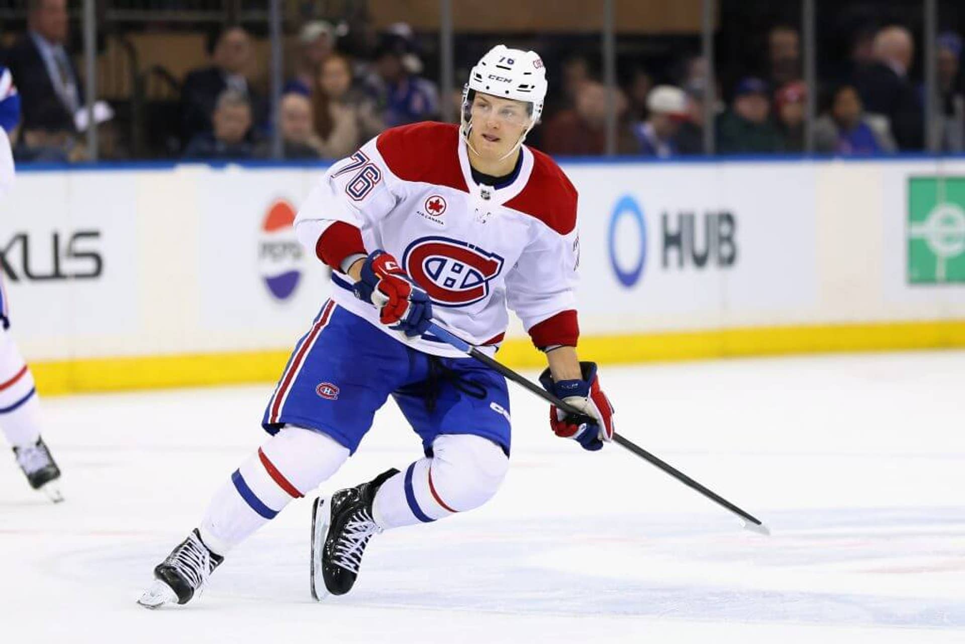 Zack Bolduc holds a hockey stick with two hands while looking at action unfolding in front of him.