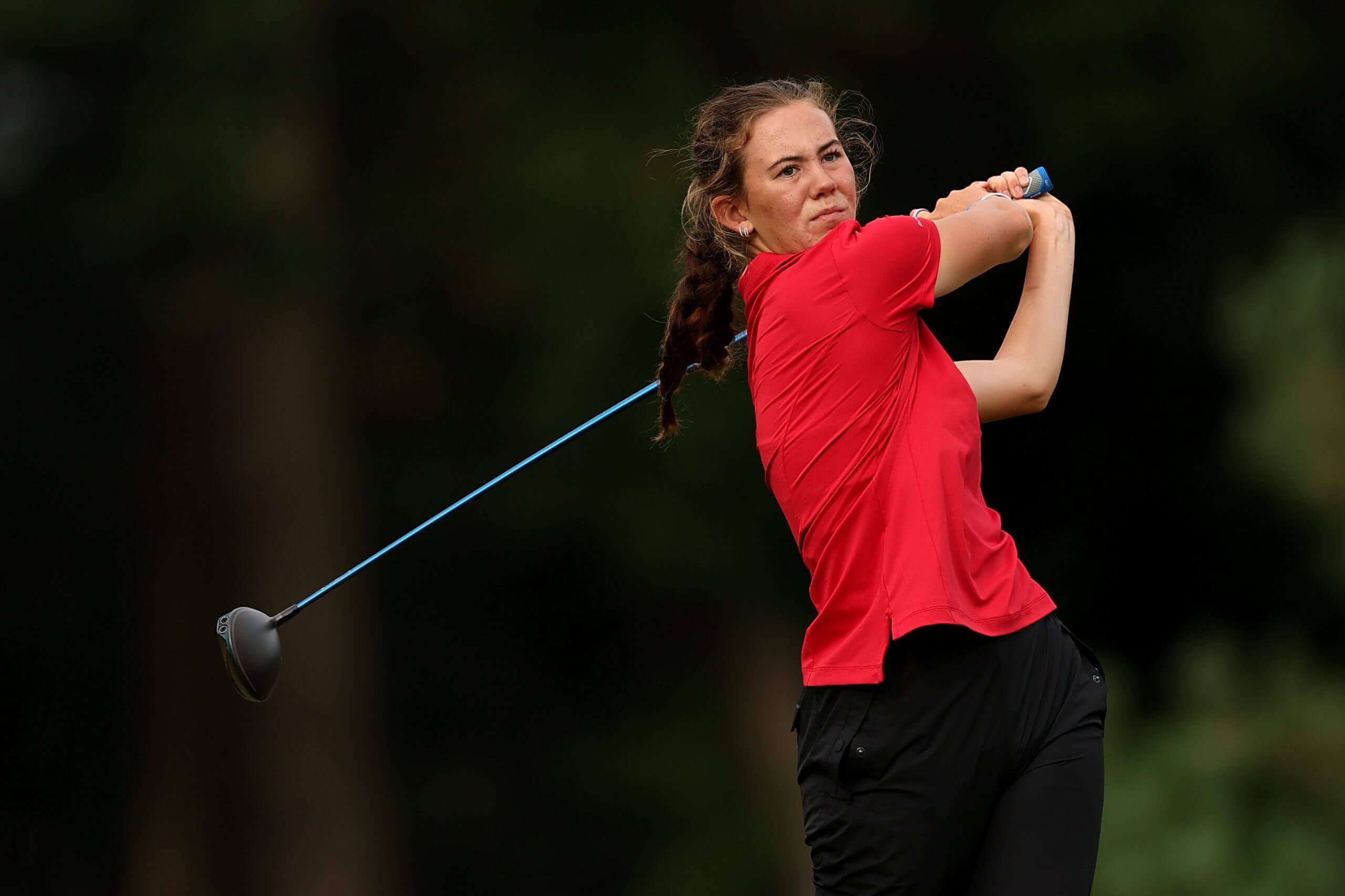 Asterisk Talley, in a red shirt and black pants, swings a blue club.