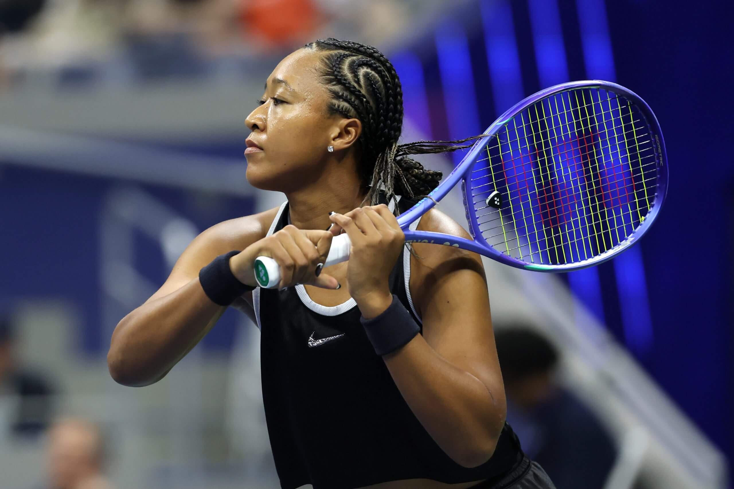 Naomi Osaka follows through on a two-handed backhand wearing a black sleeveless jersey.