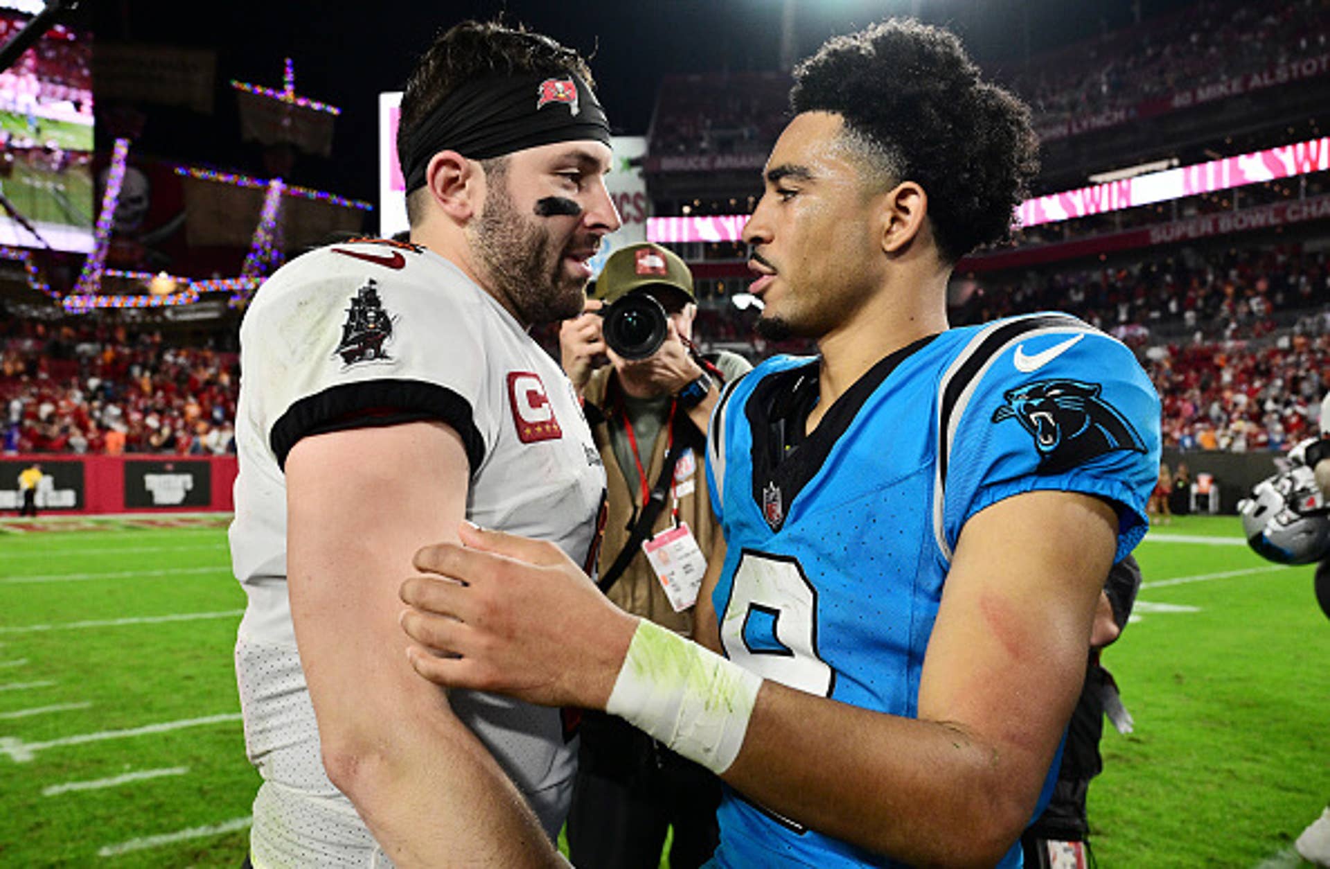 Quarterback in white uniform embraces another in a blue uniform on the field after a game.