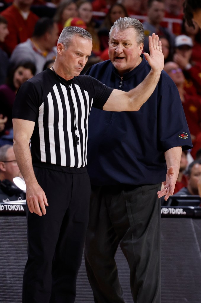 A basketball referee in a striped shirt stands next to a coach who is gesturing with his hand raised.