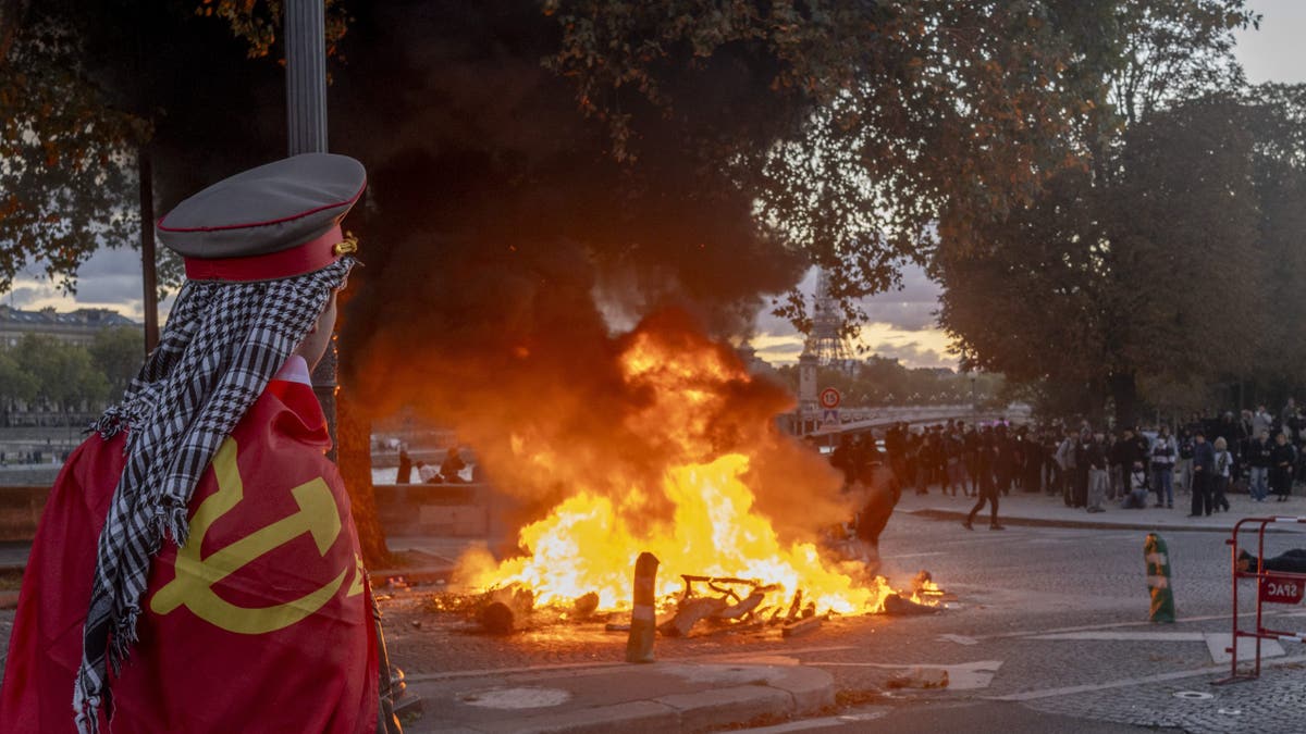 A protester watches a fire burn at a demonstration in Paris, France, on Saturday, Oct. 17, 2026. Rioters attacked French public buildings and looted stores in cities including Paris as protests against the high cost of living drew more than half a million people, underscoring the nation's challenges ahead of presidential elections next year.
